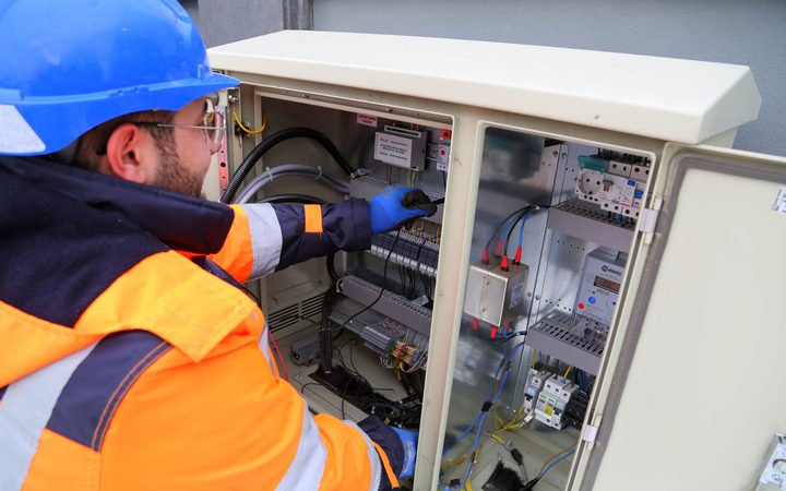 Installatiemonteur met helm en handschoenen werkt in een schakelkast